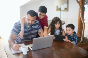 A father working on his laptop surrounded by three kids.