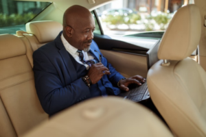 African american male in the back of a car working on his computer