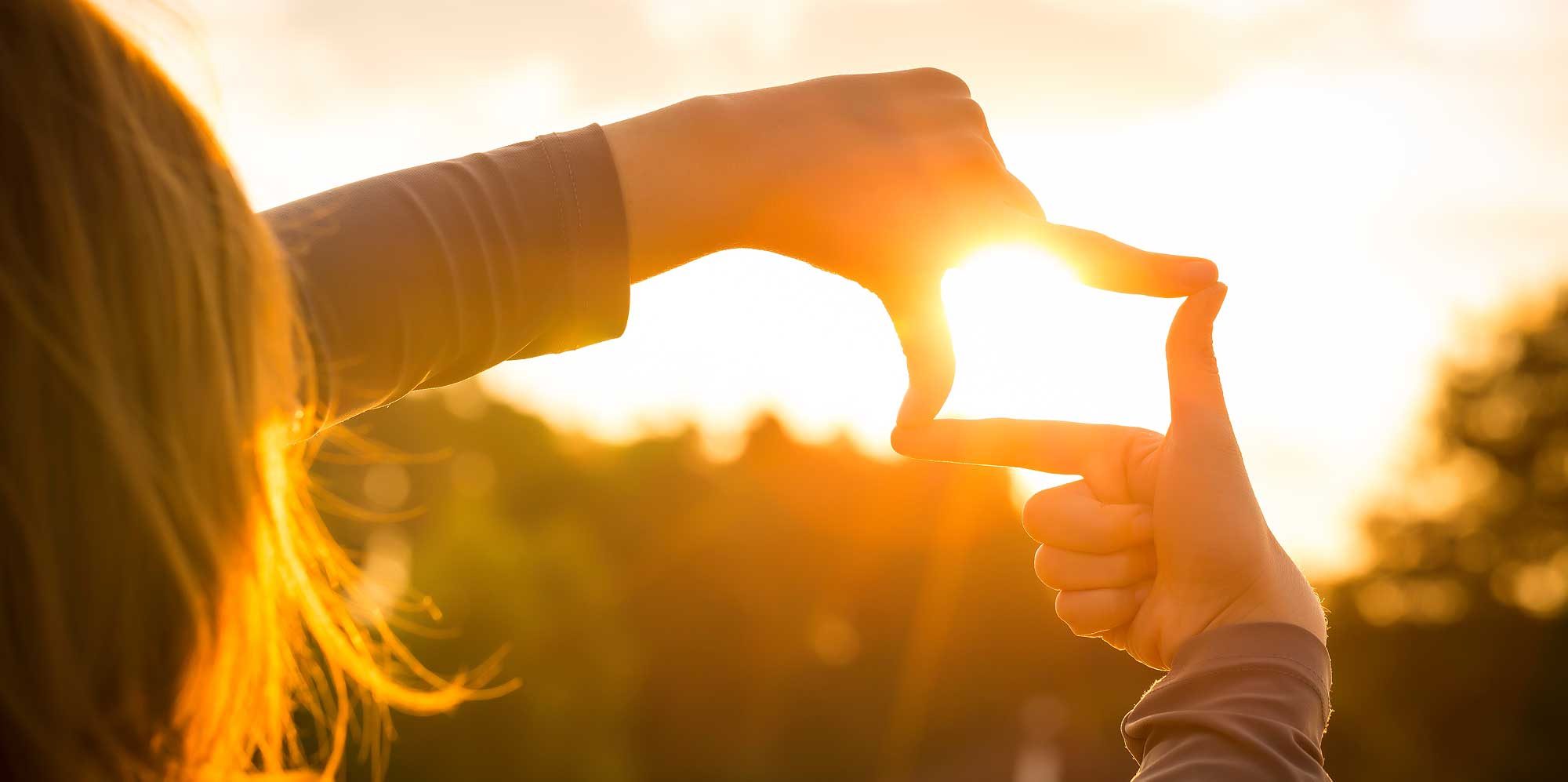 Woman using fingers to create a frame towards sunrise