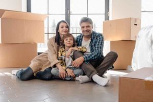 Family sitting on the floor of new apartment with moving boxes around them.