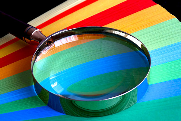 Close up of magnifying glass on rainbow colored background.