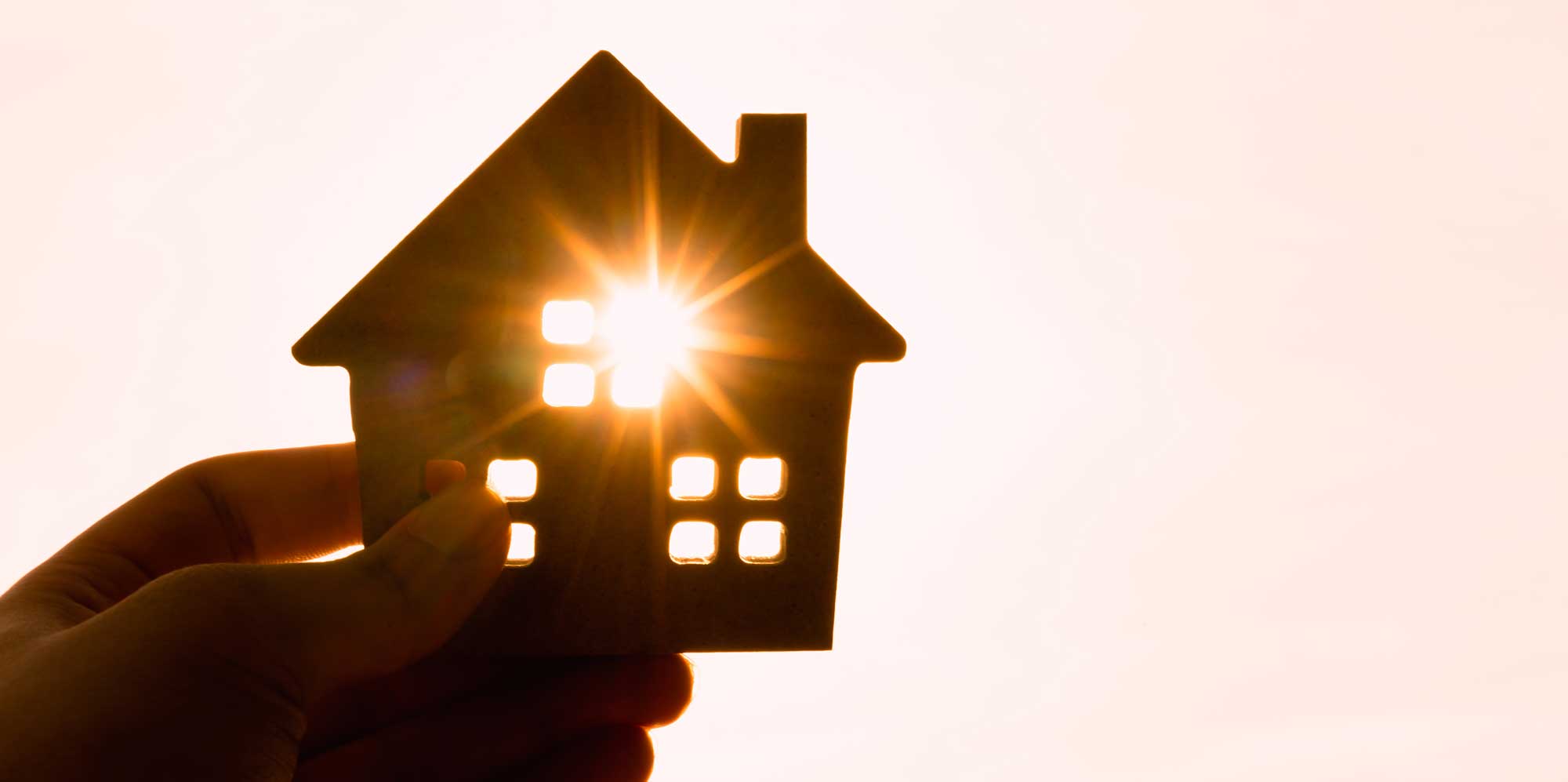 Person holding a cutout shape of a house with sun light shining through it
