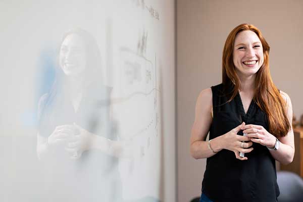smiling red headed woman standing at whiteboard